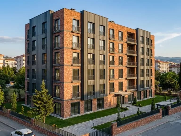Modern çok katlı konut binası; tuğla cephe, metal detaylar ve yeşil alanlarla çevrili.